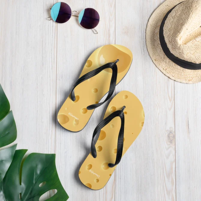 Chanclas de queso Gruyere sobre piso de madera junto a sombrero y lentes.