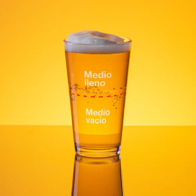 Vaso medio lleno lleno de cerveza sobre fondo amarillo.