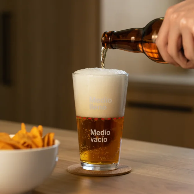 Vaso medio lleno con cerveza hasta la mitad.